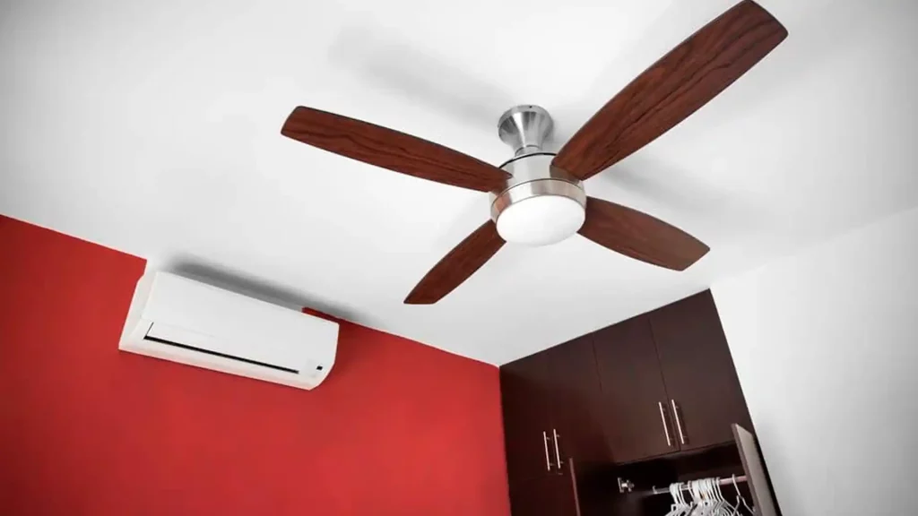 Um ventilador de teto com 4 pás marrons e um ar condicionado no fundo.