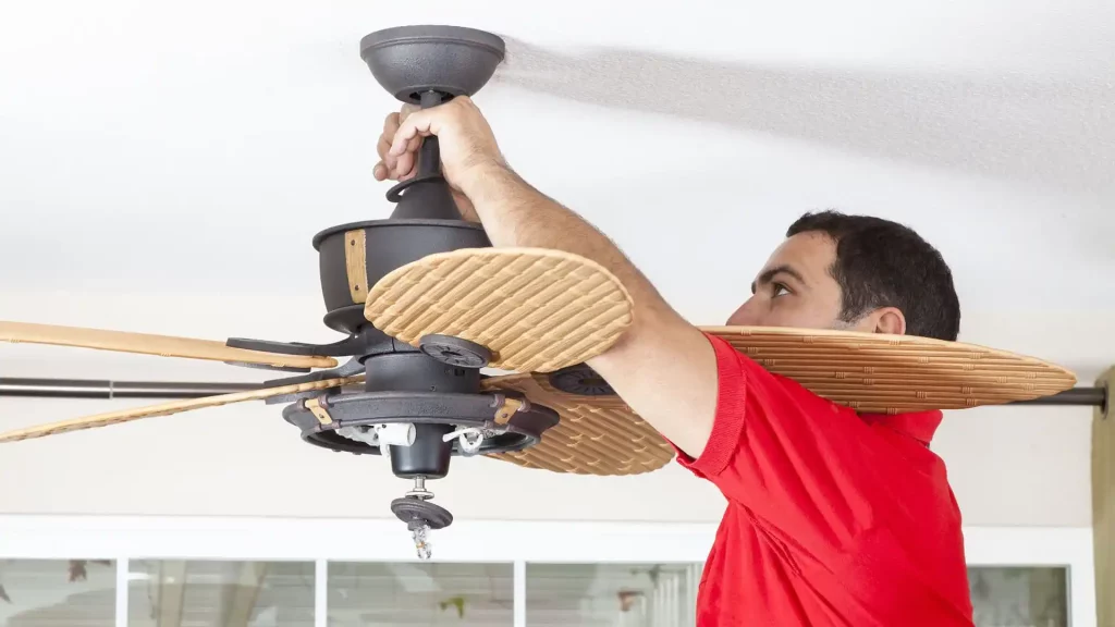 Homem com camisa vermelha instalando um ventilador de teto