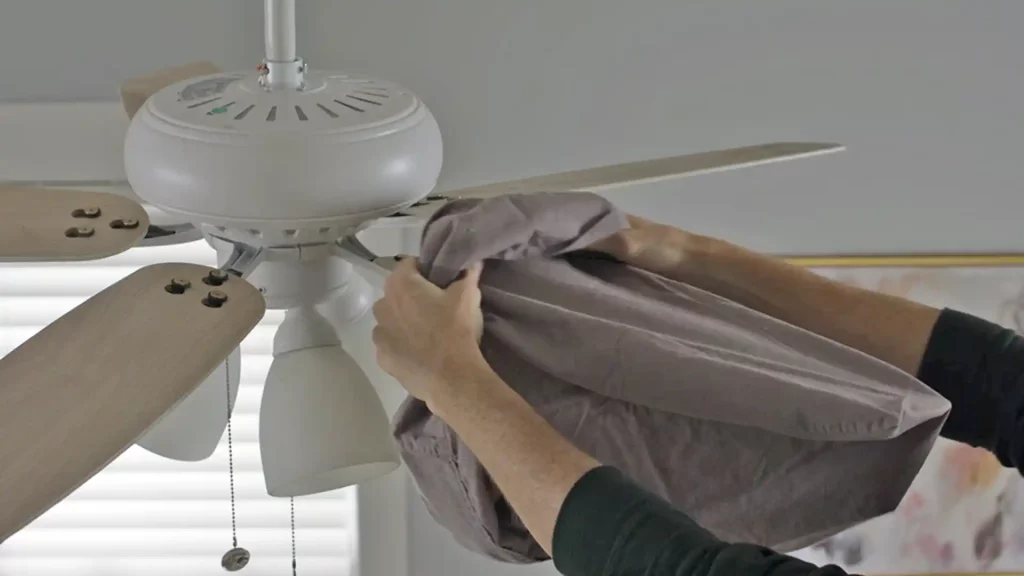 Pessoa limpando ventilador de teto com um pano macio e úmido